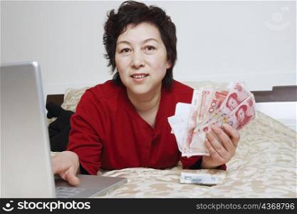 Portrait of a mature woman using a laptop holding paper currency