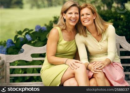Portrait of a mature woman with a mid adult woman sitting on a park bench and smiling