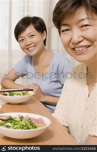 Portrait of a mature woman with her daughter sitting at a dining table and smiling