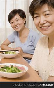 Portrait of a mature woman with her daughter sitting at a dining table and smiling
