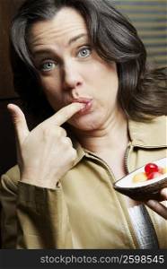 Portrait of a mature woman with her finger in her mouth and holding a tart