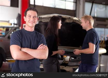 Portrait of a mechanic looking at the camera with a customer and second mechanic in the background