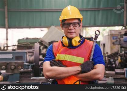 Portrait of a mechanical engineer or worker with yellow safety helmet holding the ring spanner at work in a factory.