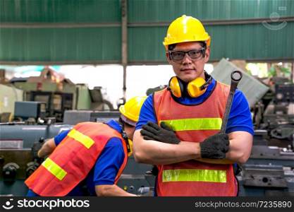 Portrait of a mechanical engineer or worker with yellow safety helmet holding the ring spanner at work in a factory. Industrial, Mechanic, Engineering Concept.