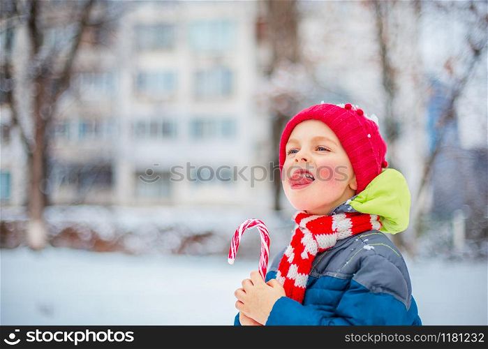 Portrait of a merry boy with christmas lollipop in hands on a winter street. Funny emotions on the face of the child.. Portrait of a merry boy with christmas lollipop in hands on a winter street.