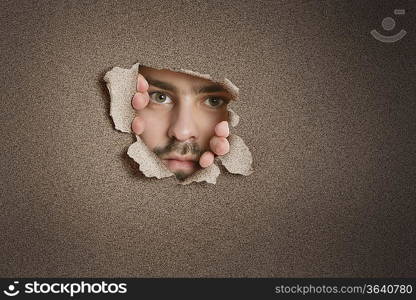 Portrait of a mid adult Caucasian man peeking from ripped paper hole