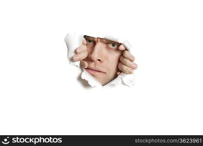 Portrait of a mid adult Caucasian man peeking from ripped white paper hole