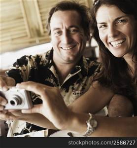 Portrait of a mid adult couple holding a digital camera in a restaurant
