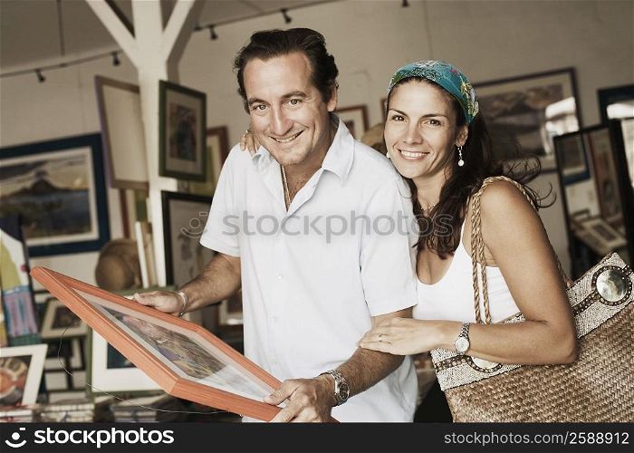 Portrait of a mid adult couple purchasing paintings from a store