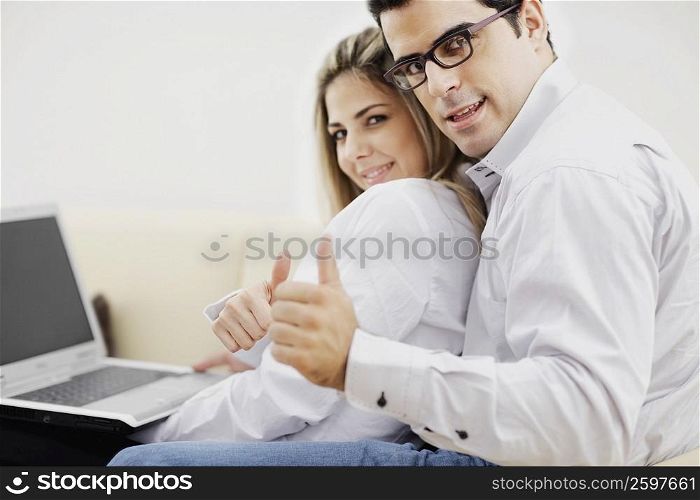 Portrait of a mid adult couple sitting in front of a laptop and showing thumbs up signs