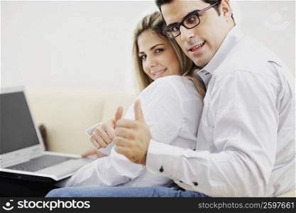 Portrait of a mid adult couple sitting in front of a laptop and showing thumbs up signs
