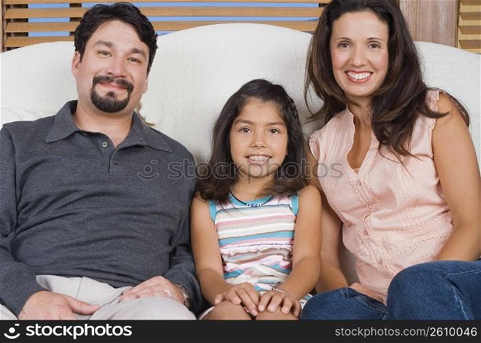 Portrait of a mid adult couple sitting on a couch with their daughter and smiling