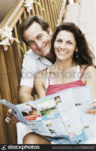 Portrait of a mid adult couple sitting on a staircase and holding a brochure