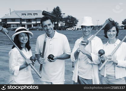 Portrait of a mid adult couple with a mature couple holding croquet mallets and balls