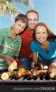 Portrait of a mid adult couple with their son in front of a barbecue grill
