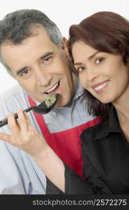 Portrait of a mid adult man and a mid adult woman tasting food with a spoon