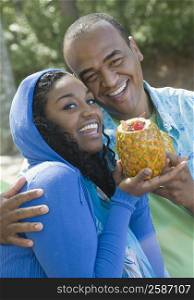 Portrait of a mid adult man and a young woman holding a pineapple and smiling
