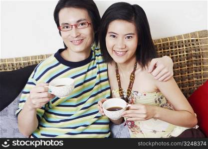 Portrait of a mid adult man and a young woman holding cups of tea and smiling