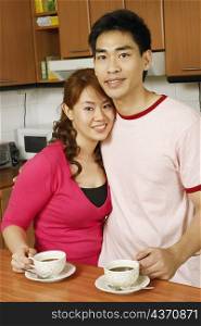Portrait of a mid adult man and a young woman holding cups of tea at a kitchen counter