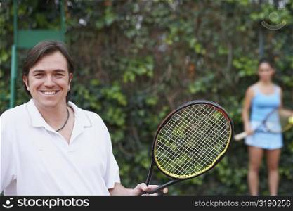 Portrait of a mid adult man and a young woman holding tennis rackets on a tennis court