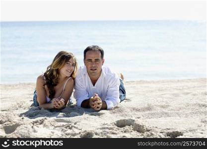 Portrait of a mid adult man and a young woman lying on the beach