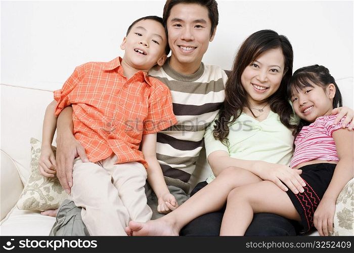 Portrait of a mid adult man and a young woman sitting on a couch with their son and daughter