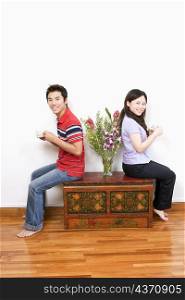 Portrait of a mid adult man and a young woman sitting on a trunk and holding cups of tea