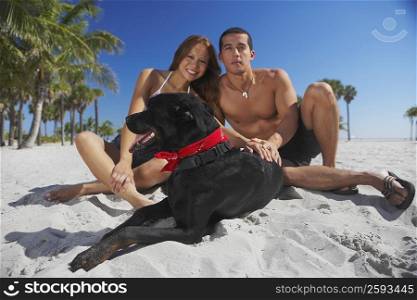 Portrait of a mid adult man and a young woman sitting with their dog on the beach