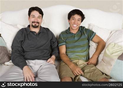 Portrait of a mid adult man and his son sitting on a couch and smiling
