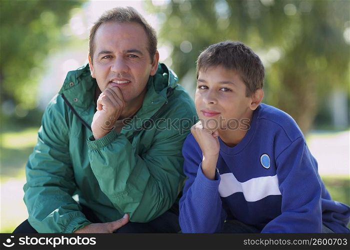 Portrait of a mid adult man and his son sitting with their hand on chin
