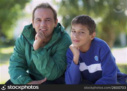 Portrait of a mid adult man and his son sitting with their hand on chin