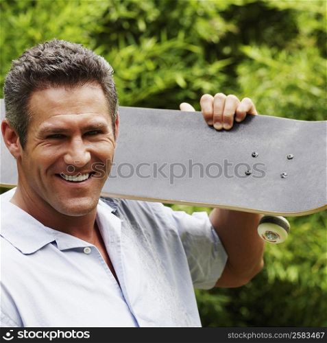 Portrait of a mid adult man carrying a skateboard on his shoulder and smiling