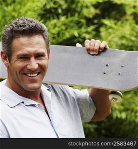 Portrait of a mid adult man carrying a skateboard on his shoulder and smiling