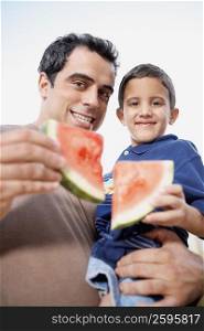 Portrait of a mid adult man carrying his son and holding slices of watermelon