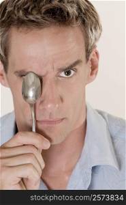 Portrait of a mid adult man covering his eye with a spoon