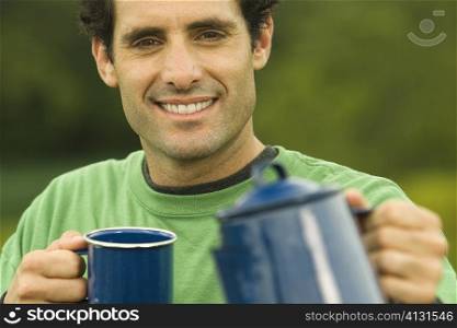 Portrait of a mid adult man holding a coffee cup and a kettle