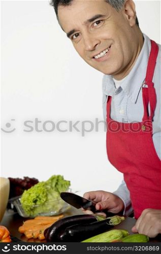 Portrait of a mid adult man holding a knife in front of vegetables