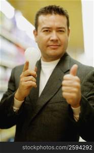 Portrait of a mid adult man holding a light bulb and showing a thumbs up sign