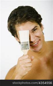 Portrait of a mid adult man holding a paintbrush in front of his face