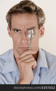 Portrait of a mid adult man holding a spoon in front of his eye