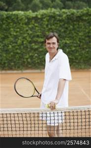 Portrait of a mid adult man holding two tennis balls and a tennis racket