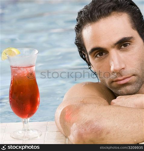 Portrait of a mid adult man leaning at the edge of a swimming pool with a cocktail