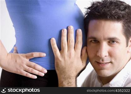 Portrait of a mid adult man listening to a pregnant young woman&acute;s abdomen