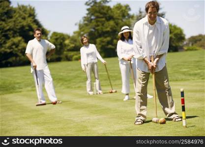 Portrait of a mid adult man playing croquet with a mature couple and mid adult woman standing behind him