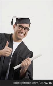 Portrait of a mid adult man showing a thumbs up sign and holding a diploma