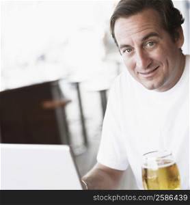 Portrait of a mid adult man sitting in front of a laptop and holding a glass of beer
