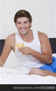 Portrait of a mid adult man sitting on the bed and holding a glass of orange juice