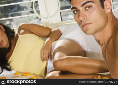 Portrait of a mid adult man sitting on the bed with a mid adult woman lying beside him