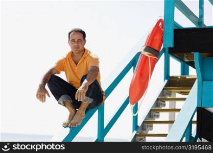 Portrait of a mid adult man sitting on the hand rail of a lifeguard hut