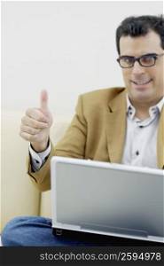 Portrait of a mid adult man sitting with a laptop and giving a thumbs up sign